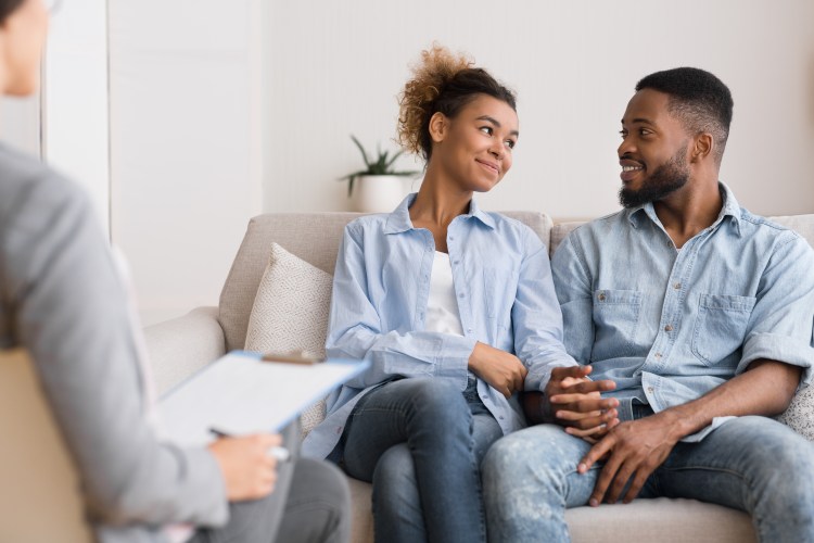Photo of a couple looking at each other and holding hands as they are talking to a therapist.