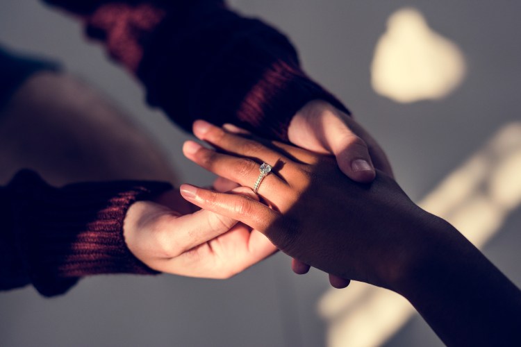 A photo of a man's hands placing a ring on a woman's finger.